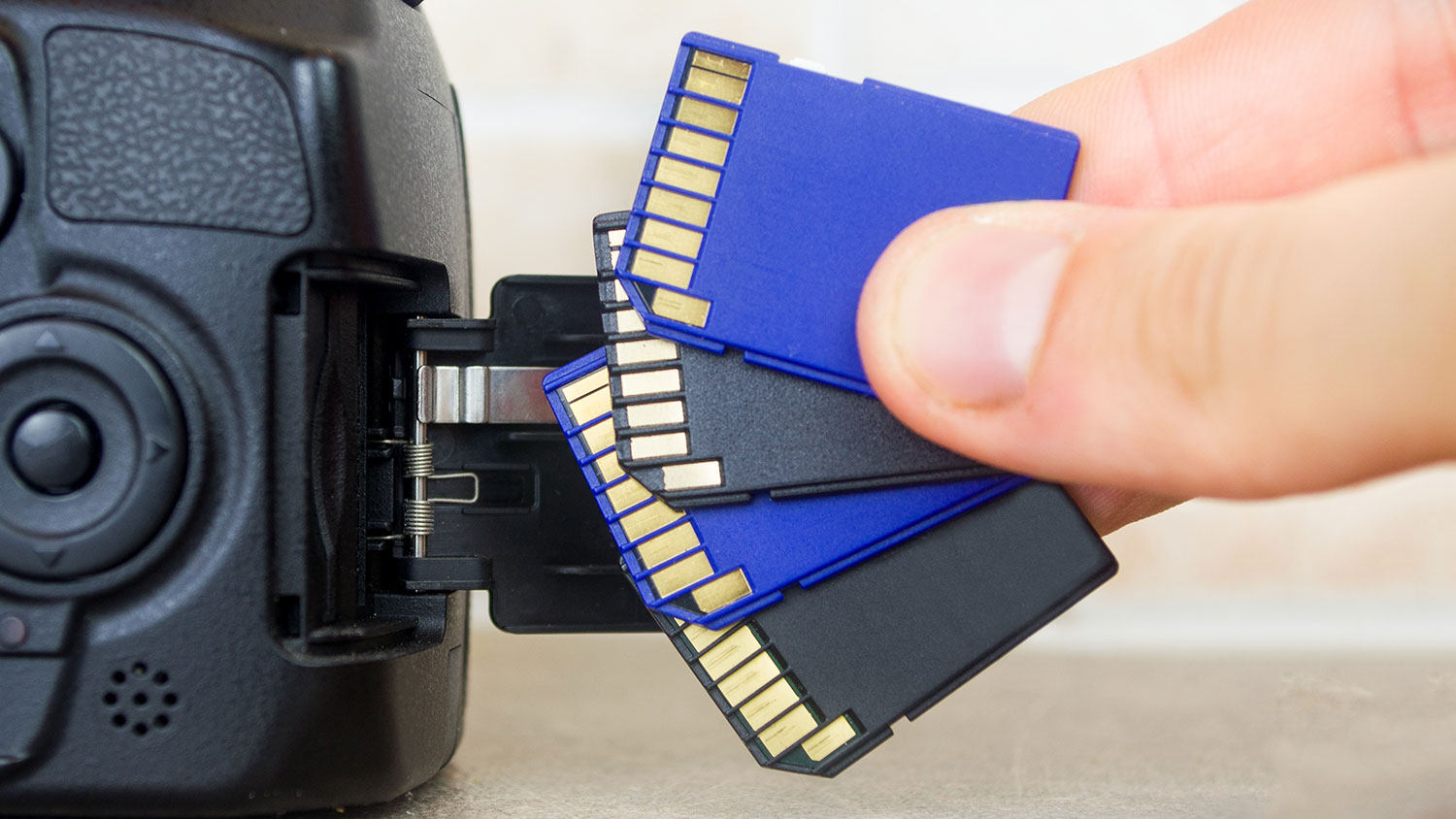 A hand holds memory cards next to a digital camera, highlighting the essential tools behind photography and content creation.