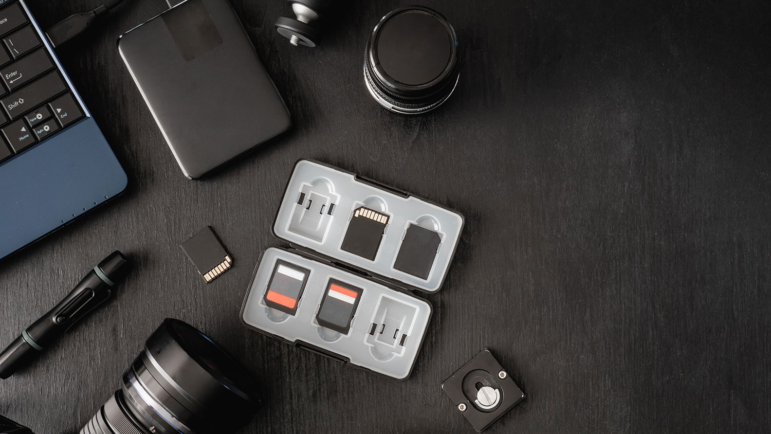 An organized camera gear kit on a surface features memory cards, batteries, a lens, and essential accessories for photographers on the go.